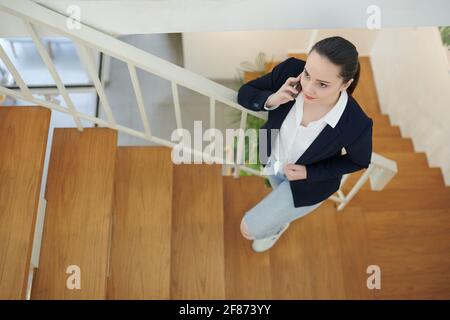 Young pretty business lady walking up the stairs in office building and calling on phone Stock Photo