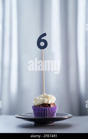 Birthday or anniversary minimalistic greeting card concept. Tasty homemade chocolate cupcake or muffin with creamy topping and number 6 six on a plate and bright background. High quality image Stock Photo