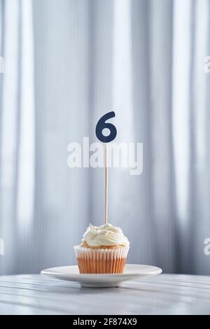 Birthday digital greeting card concept. Tasty vanilla cupcake or muffin with number 6 six on white plate with bright background. High quality vertical photo Stock Photo