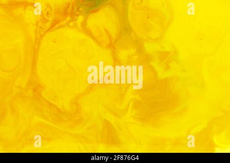 Vibrant yellow abstract amorphous background of swirling ink creating a random pattern in a full frame view for a design template Stock Photo