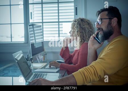 Man and woman team work together in couple at home with technology and online connection laptop computer and phone - smart working and remote workers Stock Photo