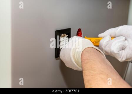 The electrician screws the roller shutters switch up and down with a yellow screwdriver in the room by the window. Stock Photo
