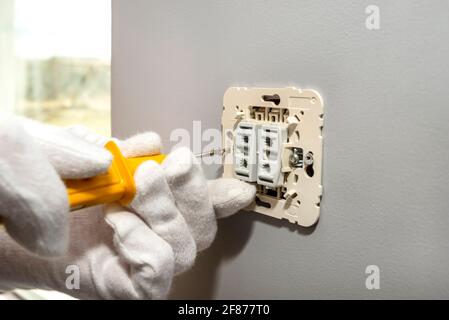 The electrician screws the roller shutters switch up and down with a yellow screwdriver in the room by the window. Stock Photo