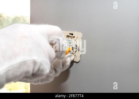 The electrician screws the roller shutters switch up and down with a yellow screwdriver in the room by the window. Stock Photo