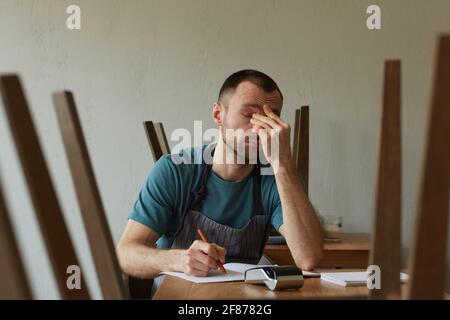 Minimal front view portrait of exhausted young man calculating finances and doing inventory at small business shop, copy space Stock Photo