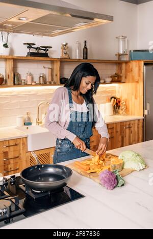Happy black woman using cutting vegetables in the kitchen at home and smiling. Stock Photo