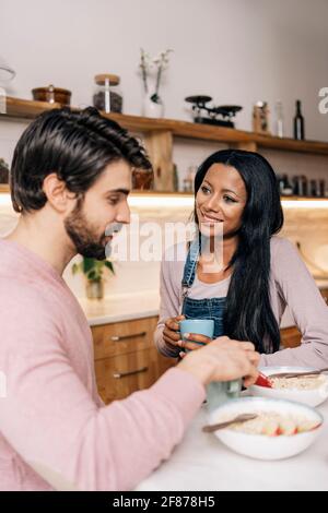 Smiley black woman and her boyfriend having delicious breakfast in the kitchen at home. Stock Photo
