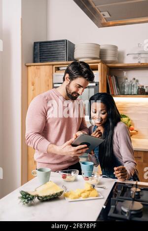 Happy couple having breakfast in the kitchen at home and using tablet. Stock Photo
