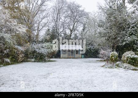 View of a suburban back garden and summerhouse in Surrey, south-east England after an unseasonal late mid-April snow covering and low temperatures Stock Photo