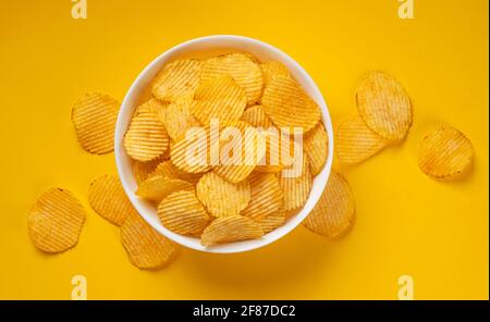 Ridged potato chips in bowl on yellow background Stock Photo