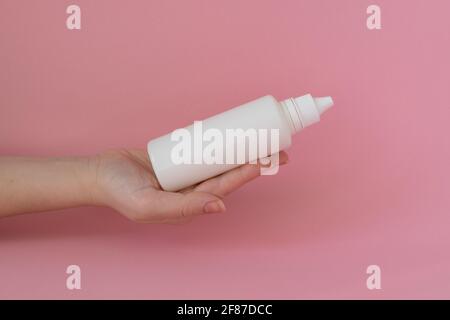 Bottle of solution in a woman's hand on pink background Stock Photo