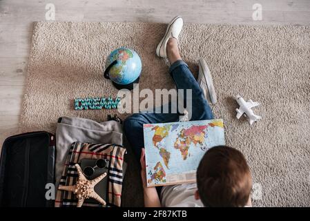 guy sitting on the floor at home with a suitcase, planning a trip, buying tickets online, traveling dreams Stock Photo