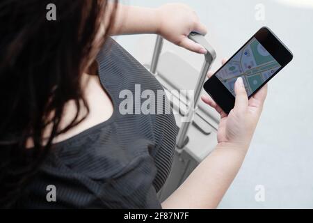 Close-up image of young woman with suitcase using smartphone to plan route to destination point Stock Photo