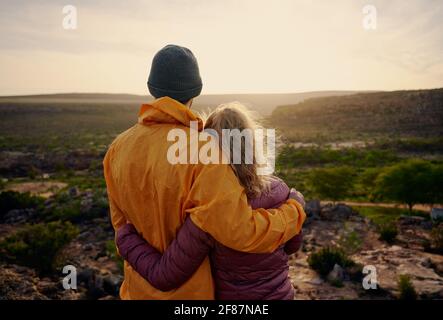 Rear view of young man and woman hugging while looking at beautiful sunrise Stock Photo