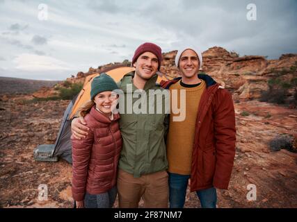 Group of young happy friends standing outside tent posing during camping in winter clothing Stock Photo