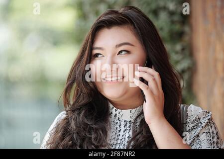 Face of beautiful smiling young mixed-race woman standing outdoors and talking on phone Stock Photo