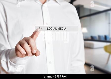 Businessman hand press the search bar icon on a virtual screen with the word social media. Stock Photo