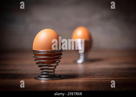 Boiled egg in a metal spiral egg cup on a wooden table. Stock Photo