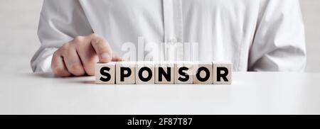 Businessman presses his finger on wooden cubes with the word sponsor. Sponsorship and financial support in business or education concept. Stock Photo