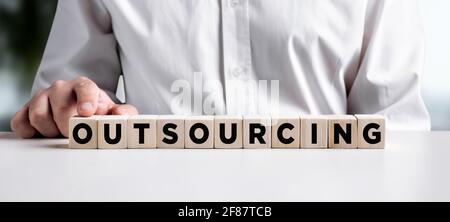 Businessman pressing his finger on the wooden cubes with the word outsourcing. Business concept. Stock Photo