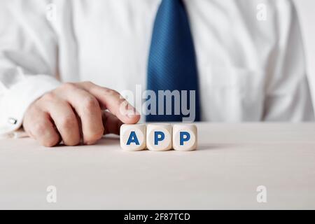 Businessman pressing his finger on the wooden cubes with the word app. Application development and communication technology. Stock Photo