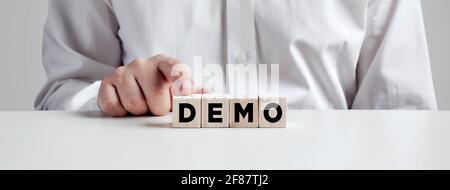Businessman pressing his finger on the wooden cubes with the word demo. Demonstration test or trial concept. Stock Photo