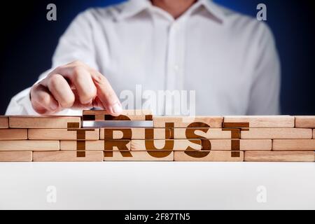 Businessman builds a structure of wooden blocks with the word trust. Building trust in business concept. Stock Photo
