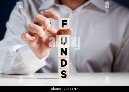 Businessman places a cube on top of tiered wooden cubes with the word funds. Increasing or growing funds in business concept. Stock Photo