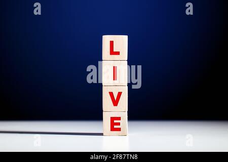 The word live written on tiered wooden cubes against blue background. Live broadcast or streaming concept. Stock Photo