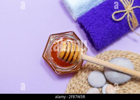 Honey spa treatment. Gold honey in a jar, towels and scented candles. Natural home skin care. Lilac background, top view. Stock Photo