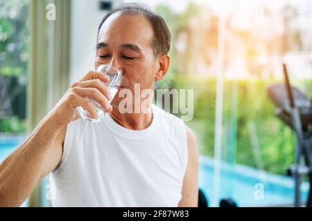Senior man drink mineral water in gym fitness center after exercise. Elderly healthy lifestyle. Stock Photo