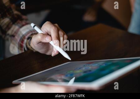 CHIANG MAI, THAILAND - FEB 26, 2020 : Hand of woman using Ipad and pencil with icons of social media on screen, smartphone life style, smartphone era Stock Photo