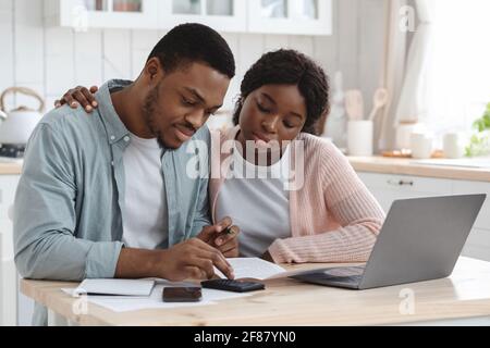 Portraif Of Young African Couple Sitting At Table In Kitchen, Reading Documents Stock Photo