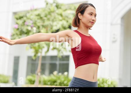 Pretty slim young Asian woman stretching and warming up before training utdoors Stock Photo
