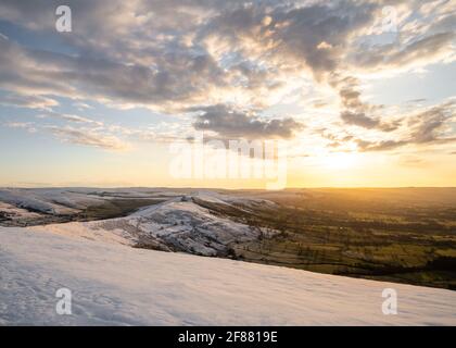 Stunning golden sunrise over snow covered hill Mam Tor mountain in Derbyshire Peak District countryside amazing sky cloudscape. Winter scene no people Stock Photo