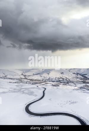 Thunder snow storm gathering over winding icy winter black road  mountains no people. Dramatic sky clouds snowy landscape near Mam Tor Edale mountain Stock Photo