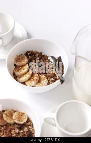 Home Breakfast Serving on White Table. Cereal Bowls with Milk Jar and Coffee Cups. Stock Photo