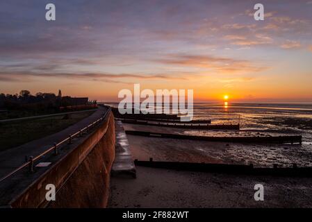 Sea defences at sunrise. Seawall above the beach at Gunners Park, Shoeburyness, Essex, UK, with breakwaters at low tide. Dawn sky Stock Photo