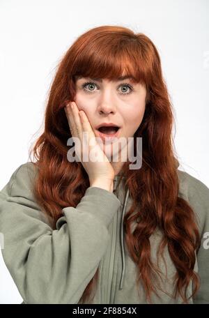 Portrait of a woman with red hair infront of white background looking surprised into camera Stock Photo