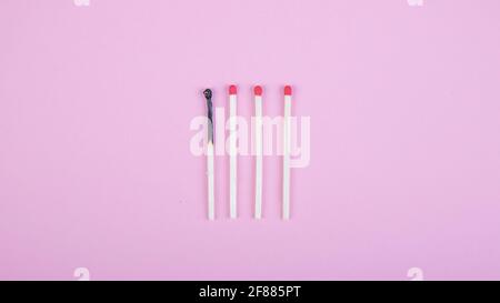 four match sticks, one burned on pink background Stock Photo