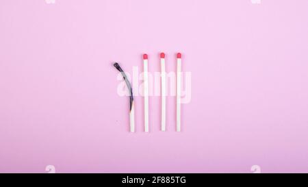 four match sticks, one burned on pink background Stock Photo