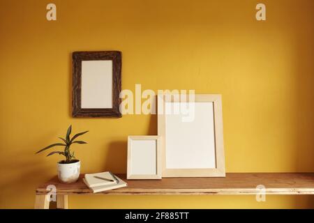 Wooden frames mockup. Flowerpot on a pile of books on an old wooden shelf. Composition on a yellow wall background Stock Photo