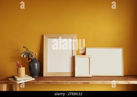 Wooden frames mockup. Composition with a flowerpot, dried artichokes, a notebook and a cup. Against the background of a yellow wall Stock Photo