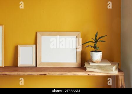 Wooden picture frames mockup. Flowerpot on a pile of books on an old wooden shelf. Composition on a yellow wall background Stock Photo