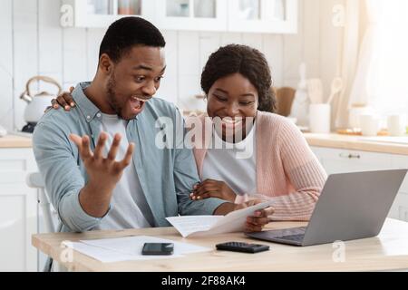 Excited black happy couple celebrating good news in kitchen, reading mail letter Stock Photo
