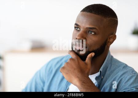 Portrait Of Thoughtful Black Millennial Man Touching Chin And Looking Away Stock Photo