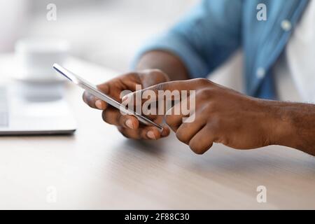 Cropped Image Of Unrecognizable Black Man Using Smartphone While Sitting At Desk Stock Photo