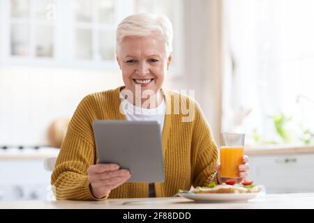 Smiling senior woman having lunch and using digital tablet Stock Photo