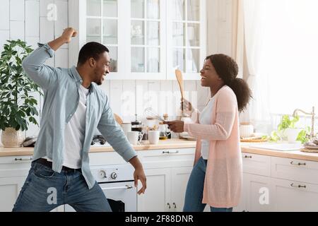 Domestic Fun. Black spouses playfully fighting in kitchen, using spatulas as weapons Stock Photo
