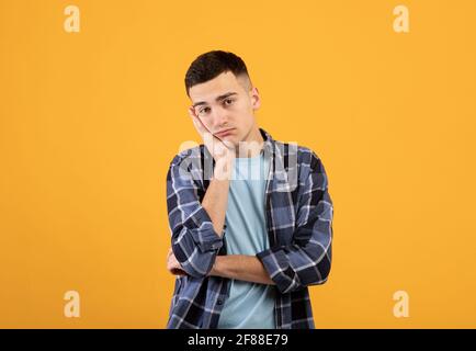 Portrait of young guy feeling bored, leaning on his hand, having dull day on orange studio background Stock Photo